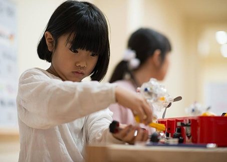 ロボット工作キットの部品を手に取って組み立てる児童